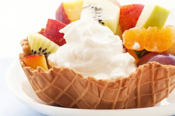 Eine Waffelschale ist gefüllt mit frischen Früchten und einer großzügigen Portion Sahne, perfekt für ein schnelles Dessert.