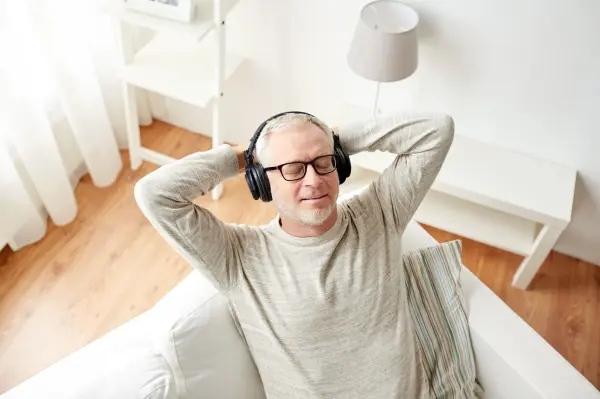 Ein Mann sitzt entspannt auf einer Couch, trägt Kopfhörer und genießt die ruhige Atmosphäre des sonnigen Raums.