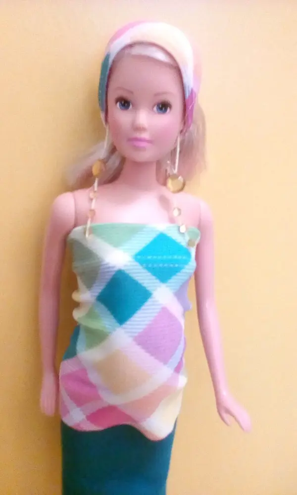 Eine Barbie-Puppe trägt ein farbenfrohes Outfit und Ohrringe, während sie vor einem gelben Hintergrund steht.