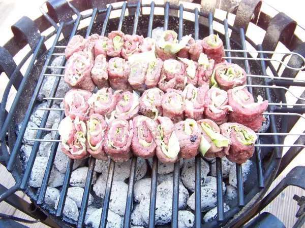 Gegrillte Rinderfilet-Rouladen liegen auf dem Grill, während sie über glühenden Kohlen zubereitet werden.