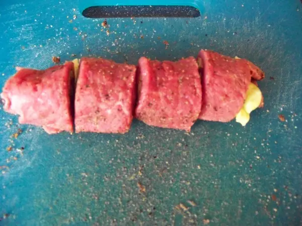 Eine gegrillte Rinderfilet-Roulade liegt auf einem blauen Schneidebrett, in Stücke geschnitten und bereit zum Servieren.