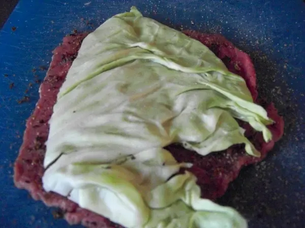 Eine Rinderfilet-Roulade wird mit grünem Spitzkohl auf einem blauen Schneidebrett vorbereitet.