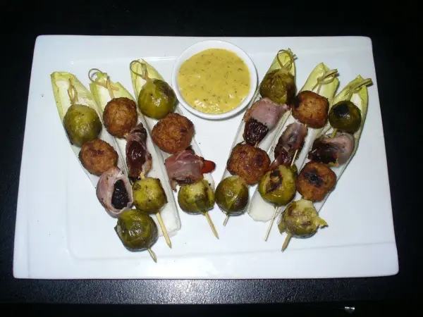 Spieße mit Hackbällchen und Rosenkohl sind auf einem weißen Teller angerichtet, umgeben von einer köstlichen Dip-Sauce.