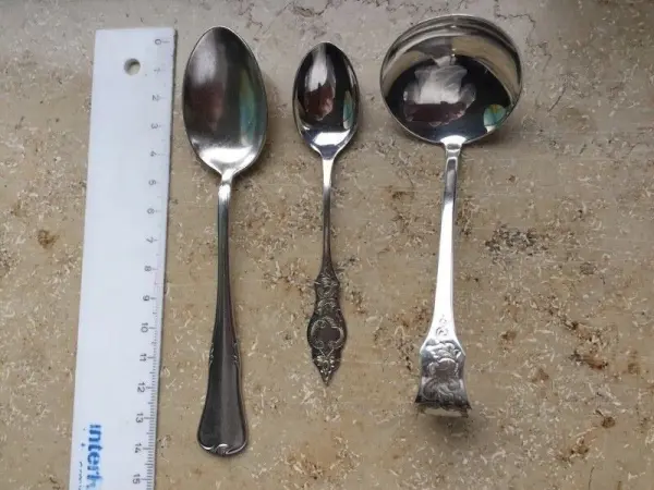 Ein Satz kleiner Teelöffel liegt neben einem Lineal auf einer hellen Oberfläche, bereit zum Portionieren von Gewürzen.