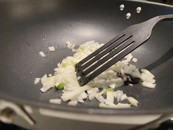 In einer Pfanne werden fein gehackte Zwiebeln mit einem Spatel angedünstet, bereit für die nächste Kochstufe.