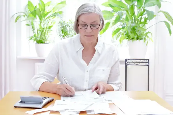 Eine Frau sitzt an einem Tisch und überprüft Belege für die Steuererklärung, um sie auf Anfrage zu sortieren.