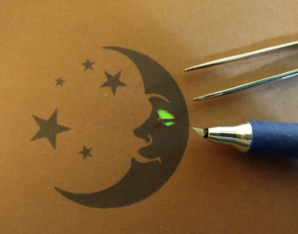 Ein Stift zeichnet eine Mond- und Sternen-Silhouette auf braunem Papier, um ein Windlicht "Fee im Glas" zu gestalten.