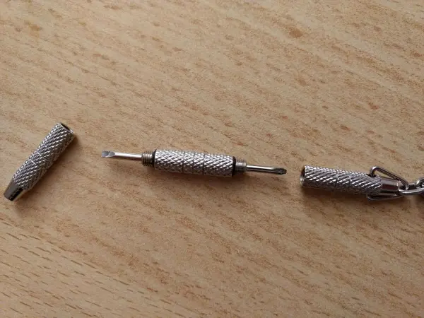 Ein zwei-in-einem Schraubendreher für Brillen liegt auf einem Holzuntergrund, bereit zur Nutzung und Reparatur von Brillen.