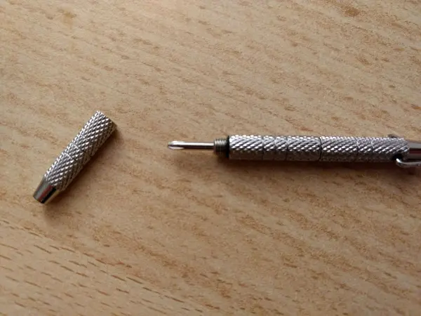 Ein Schraubendreher für Brillen liegt auf einem Holztisch, wobei der abnehmbare Kopf neben dem Griff platziert ist.