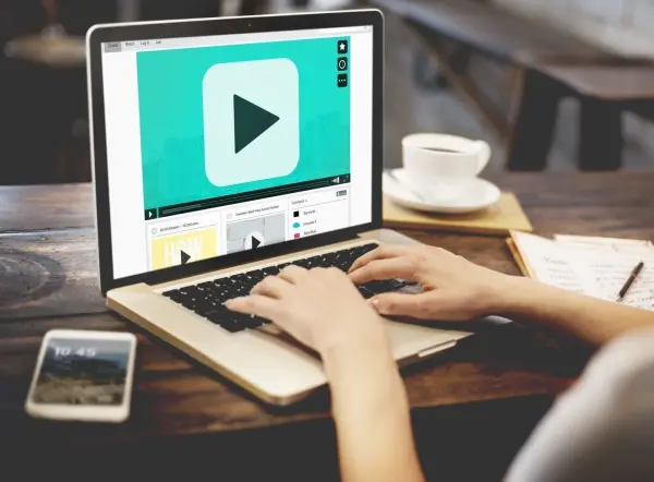 Eine Person sitzt am Tisch und spielt ein Video auf einem Laptop langsamer ab, während eine Tasse Kaffee daneben steht.