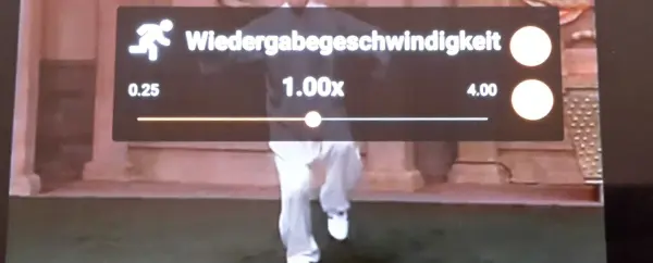 Wiedergabegeschwindigkeit wird auf 1.00x eingestellt, während jemand im Hintergrund langsamer läuft.