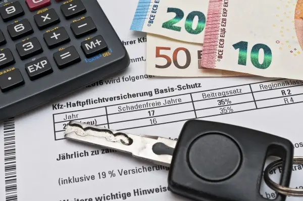 Ein Schlüssel und eine Geldbörse liegen auf einem Versicherungsvertrag, während ein Taschenrechner daneben steht.