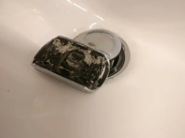 Eine benutzte Reinigungskartusche für einen Rasierer liegt schmutzig in einem Waschbecken, umgeben von Wasser.