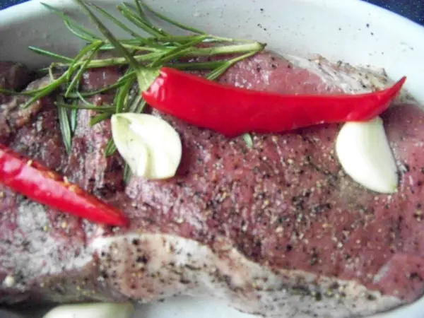 Auf einem Teller liegt ein Stück Roastbeef vom Limousin Rind, umgeben von Knoblauchzehen, rotem Pfeffer und frischen Kräutern.