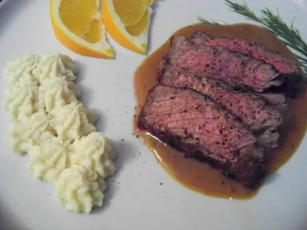 Saftiges Roastbeef vom Limousin Rind, in Scheiben geschnitten, serviert mit cremigem Kartoffelpüree und Orangenscheiben.