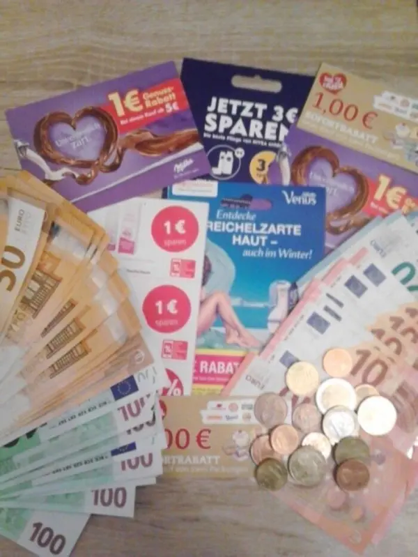 Eine Vielzahl von Geldscheinen, Münzen und Coupons liegt auf einer Oberfläche, die den Akt des Sparens verdeutlicht.