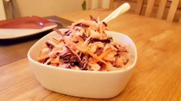 Cremiger Krautsalat befindet sich in einer weißen Schüssel auf einem Holztisch und sieht frisch zubereitet aus.