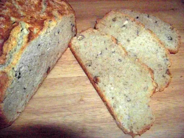 Ein frisch gebackenes Buttermilchbrot mit Nüssen liegt auf einem Holzbrett, mit mehreren geschnittenen Scheiben daneben.
