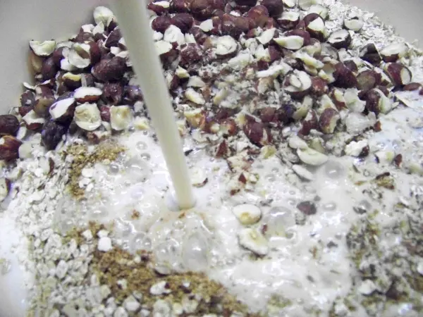 In einer Schüssel fließt Buttermilch über eine Mischung aus grob gehackten Nüssen und verschiedenen Mehlen, die bereit sind für ein Brot.