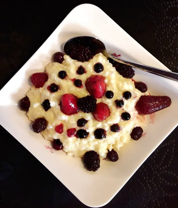 Cremiger Milchreis wird in einer weißen Schale serviert, dekoriert mit frischen Beeren, die farbenfroh angeordnet sind.