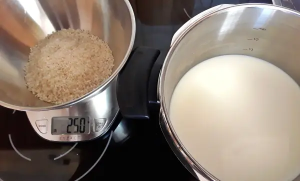 Ein Behälter mit Reis steht auf einer Waage, während daneben ein Topf mit Milch auf dem Herd wartet.