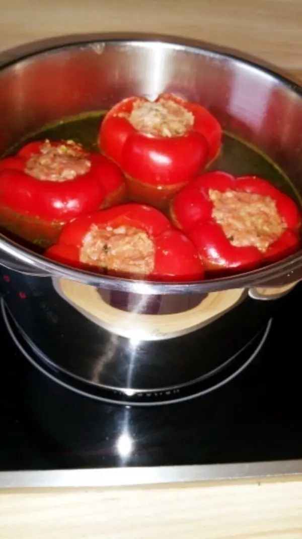 Rote Paprika sind im Schnellkochtopf gefüllt mit einer Mischung und garen in einer klaren Brühe auf dem Herd.