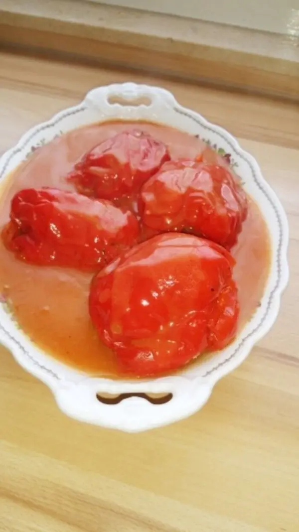 Gefüllte Paprika liegen in einer weißen Schüssel in einer schmackhaften Tomatensauce auf einem Holzuntergrund.