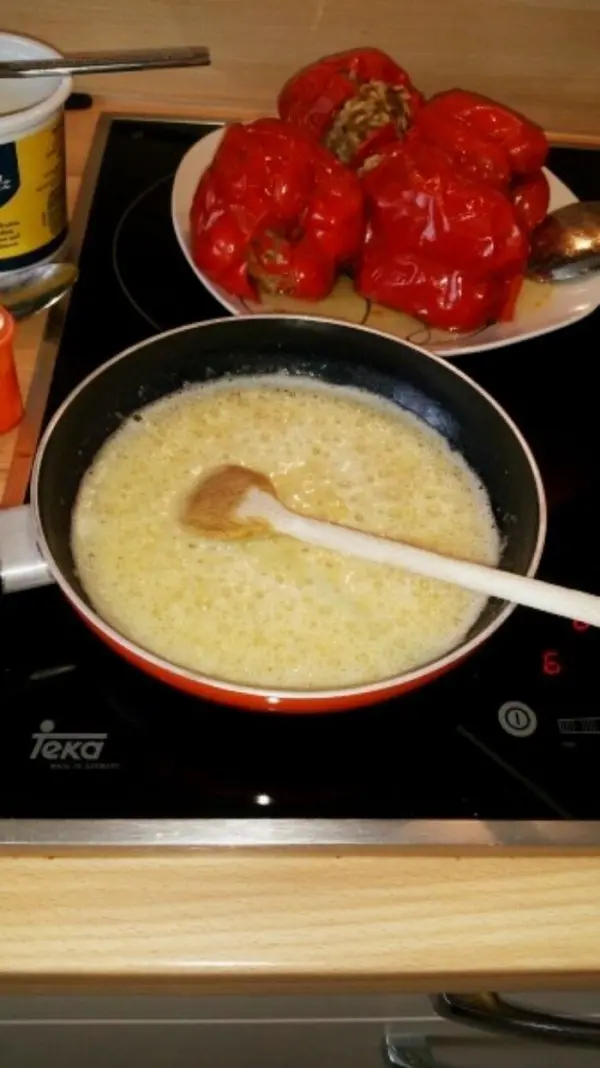 In einer Pfanne kochen gefüllte Paprika in einer würzigen Sauce, während sie auf einem Herd in einer modernen Küche platziert sind.