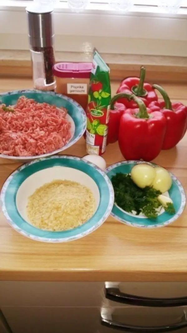 Rote Paprika und Zutaten wie Hackfleisch und Reis liegen auf einer Arbeitsfläche zur Zubereitung von gefüllten Paprika.