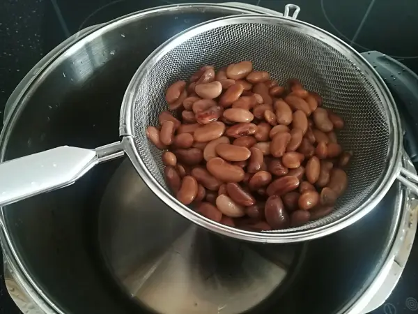 Getrocknete Bohnen liegen in einem Sieb über einem Topf und werden nach dem Kochen abgetropft.