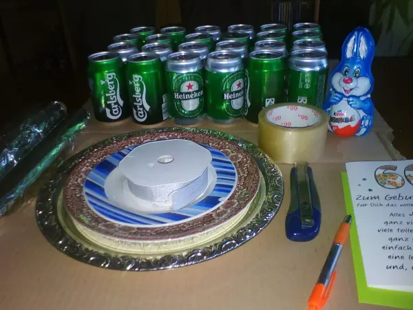 Eine Sammlung von Bierdosen und Zubehör liegt bereit, um eine kreative Biertorte für einen Mann zu gestalten.