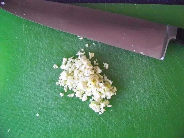 Auf einem grünen Schneidebrett liegt fein gehackter Ingwer neben einem großen Küchenmesser, bereit für die Zubereitung von Jiachang Doufu.