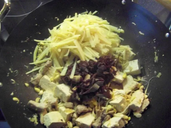 In einer Pfanne liegen frischer Jiachang Doufu zusammen mit Ingwer, Pilzen und anderen Zutaten, die zubereitet werden.