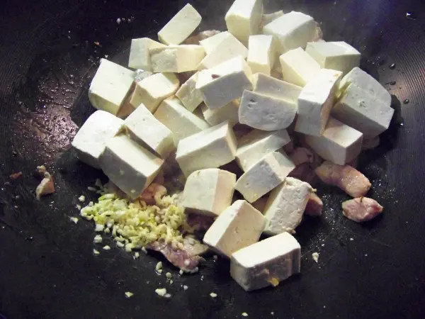 Würfel aus Tofu liegen auf einer heißen Pfanne, während sie mit Ingwer und anderen Zutaten zum Braten vorbereitet werden.