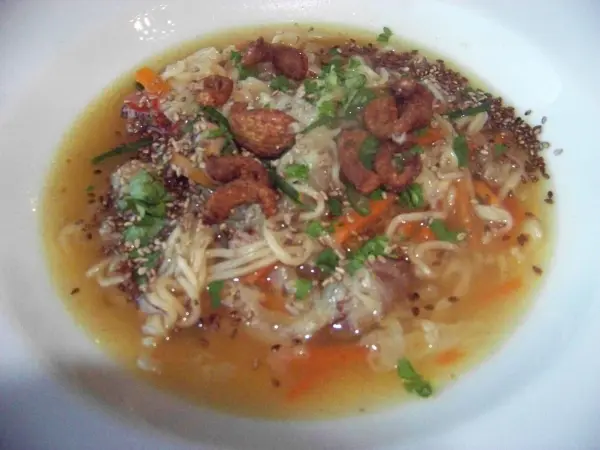 In einer weißen Schüssel liegt eine leckere Chinakohlsuppe, die mit Entenbrust, Gemüse und knusprigen Einlagen garniert ist.