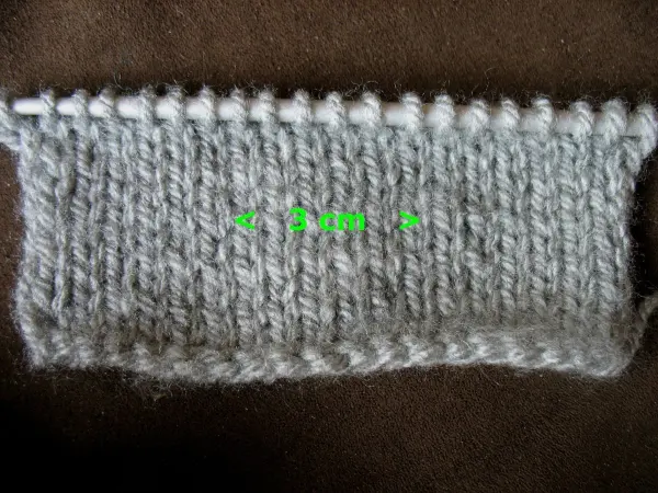 Ein graues, selbst gestricktes Stirnband liegt auf einem dunklen Hintergrund und zeigt die charakteristische Maschenstruktur.