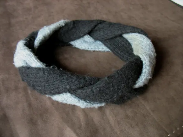 Ein selbst gestricktes Stirnband liegt auf einem braunen Untergrund, kunstvoll geflochten in Grau und Hellblau.