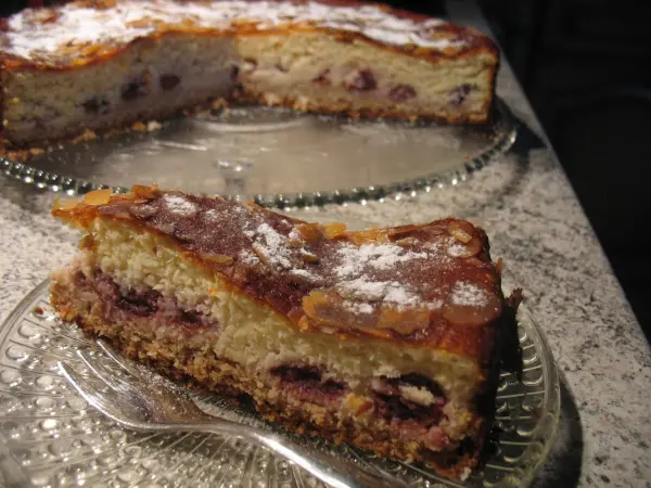 Eine Quark-Sahne-Kirsch-Torte mit Kokosgeschmack ist auf einem schönen Glasuntersetzer zu sehen. Ein Stück ist auf einem weiteren Teller platziert.