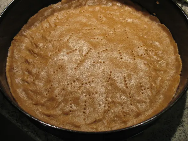 Ein runder Kuchenboden liegt in einer Backform und wartet darauf, mit Quark und Kirschen für die Torte dekoriert zu werden.