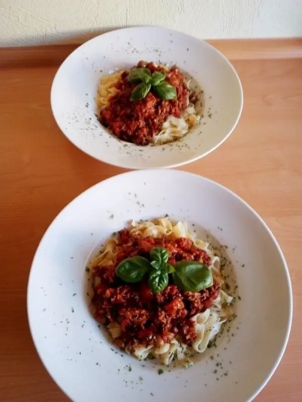 Zwei Teller mit Bandnudeln sind mit einer üppigen Bolognese-Sauce und frischem Basilikum garniert, auf einem Holztisch.