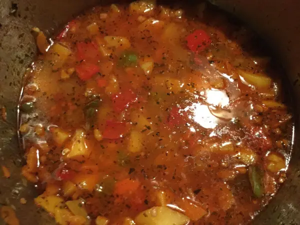 Ein schmackhaftes Kartoffelgulasch kocht in einem Topf, umgeben von frischen, bunten Gemüsesorten in einer würzigen Brühe.