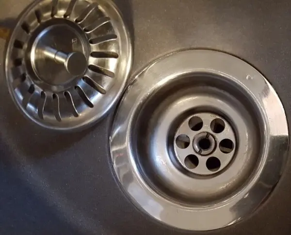Ein Abflusssieb liegt neben einem Waschbecken. Es wird gereinigt, um Verstopfungen zu vermeiden und den Wasserfluss zu sichern.