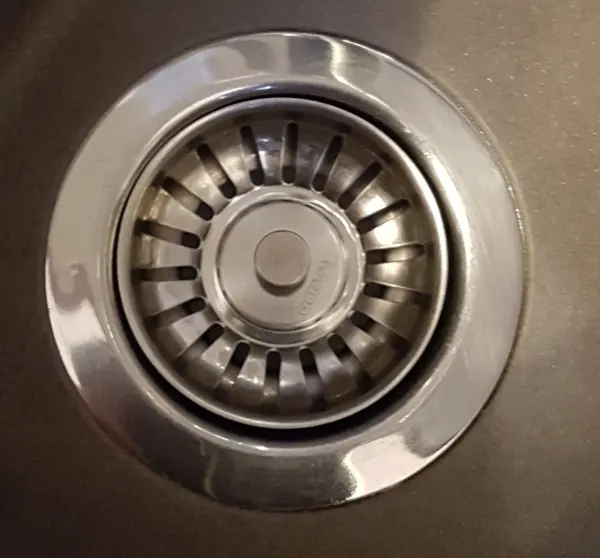 Ein metallisches Abflusssieb ist in einem Waschbecken installiert und zeigt die Struktur, die Schmutz auffängt und das Wasser durchlässt.