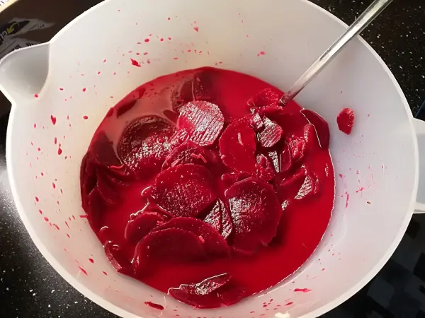 Rote Rüben liegen in einer Schüssel mit rotem Saft, während ein Löffel darin rührt, um den Salat vorzubereiten.