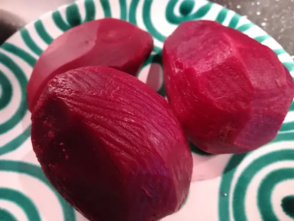 Drei geschälte rote Rüben liegen auf einem grünen, spiralförmig gemusterten Teller, bereit zum Kochen für den Salat.