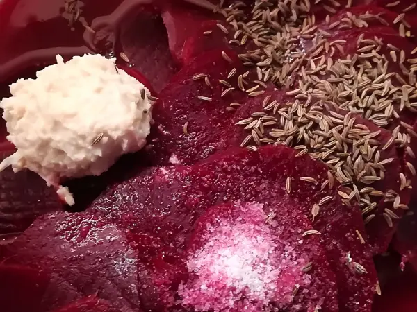 Rote Rüben liegen in einer Schüssel und werden mit Kümmel, Salz und einer cremigen Zutat zubereitet.