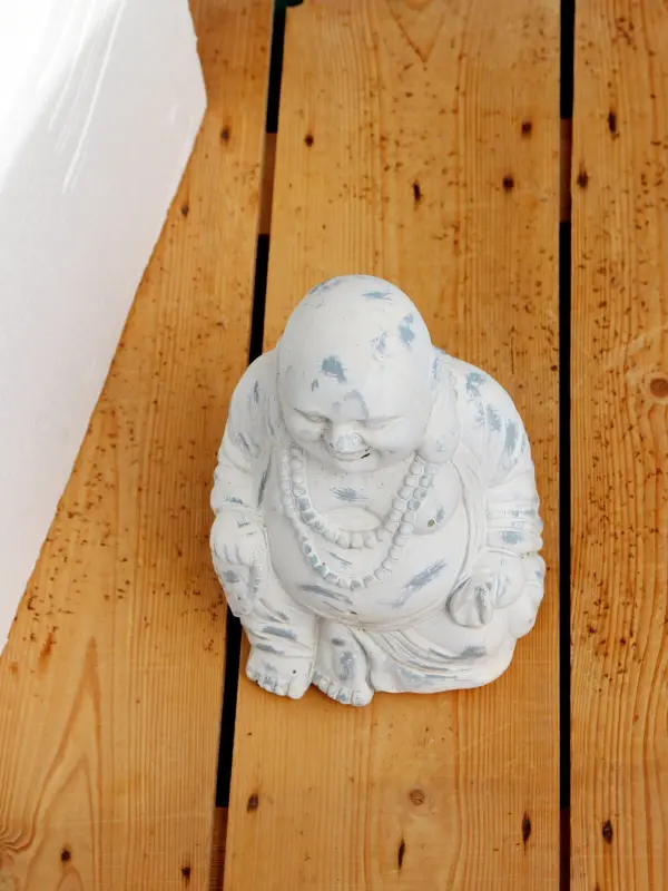 Ein Buddha-Statuette sitzt auf einem Holzboden, umgeben von einer hellen, minimalistischen Umgebung, die Ruhe ausstrahlt.