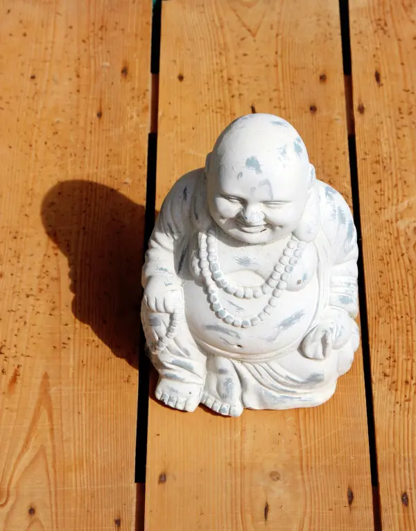Eine Buddha-Statue sitzt auf einem Holztisch und lässt einen sanften Schatten auf die Holzoberfläche fallen.
