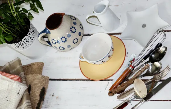 Eine stilvolle Kaffeetasse steht auf einem farbigen Untersetzer, während Löffel und eine Kanne auf einem Holztisch liegen.