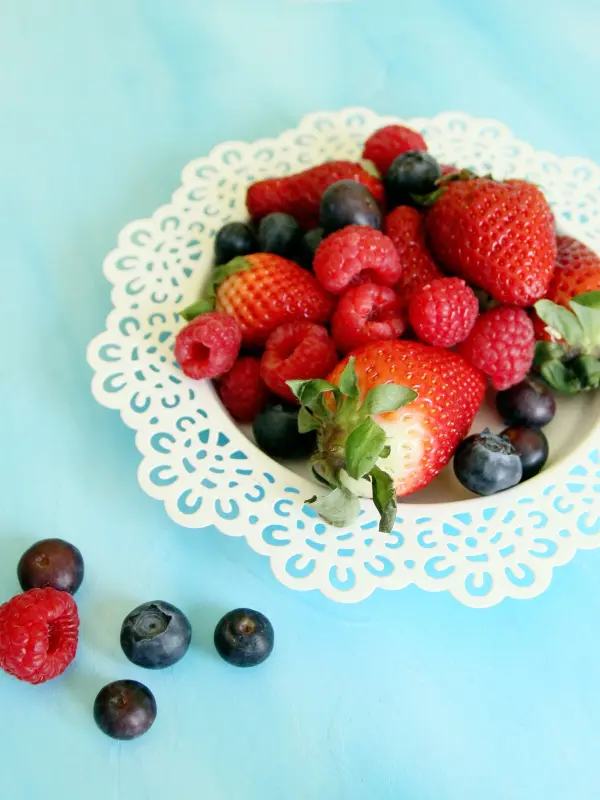 Frische Beeren in einer dekorativen Schale liegen auf einem hellblauen Tisch, ideal für Fotografie von Rezepten.